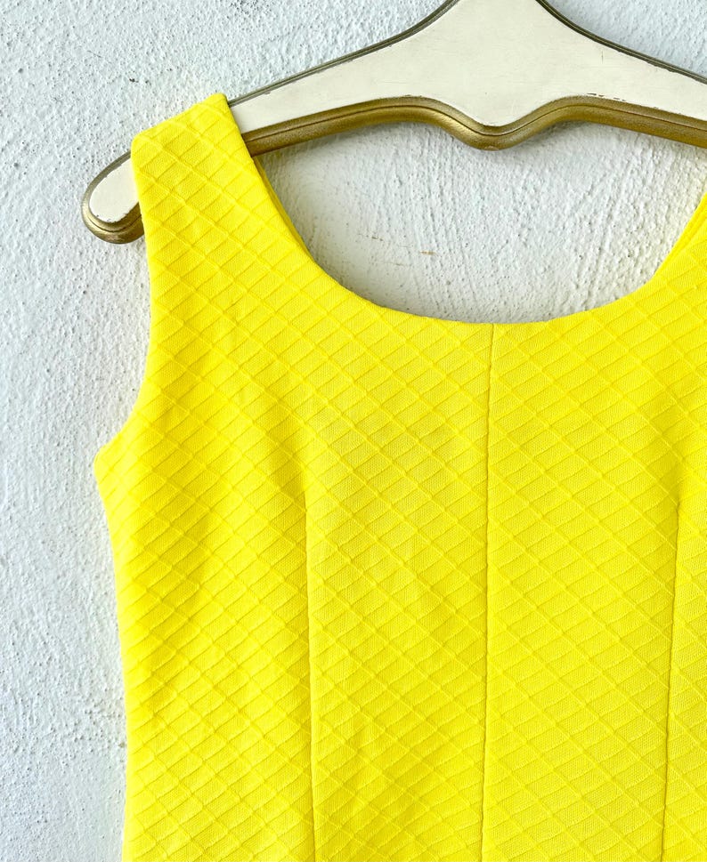Pu&ograve; includere: Un abito giallo senza maniche con un motivo a rombi. L'abito ha una scollatura rotonda ed &egrave; realizzato in un tessuto strutturato.