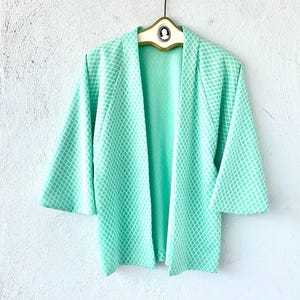 May include: A mint green kimono with a white geometric pattern. The kimono has a wide collar and long sleeves.