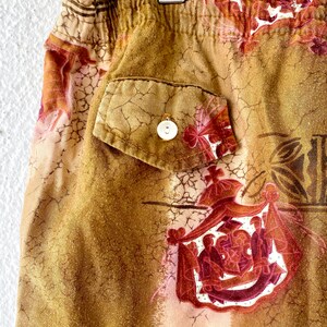 May include: Close-up of a pair of shorts with an elastic waistband and a single pocket. The shorts feature a brown and tan floral pattern with a white button on the pocket. The fabric has a textured appearance.