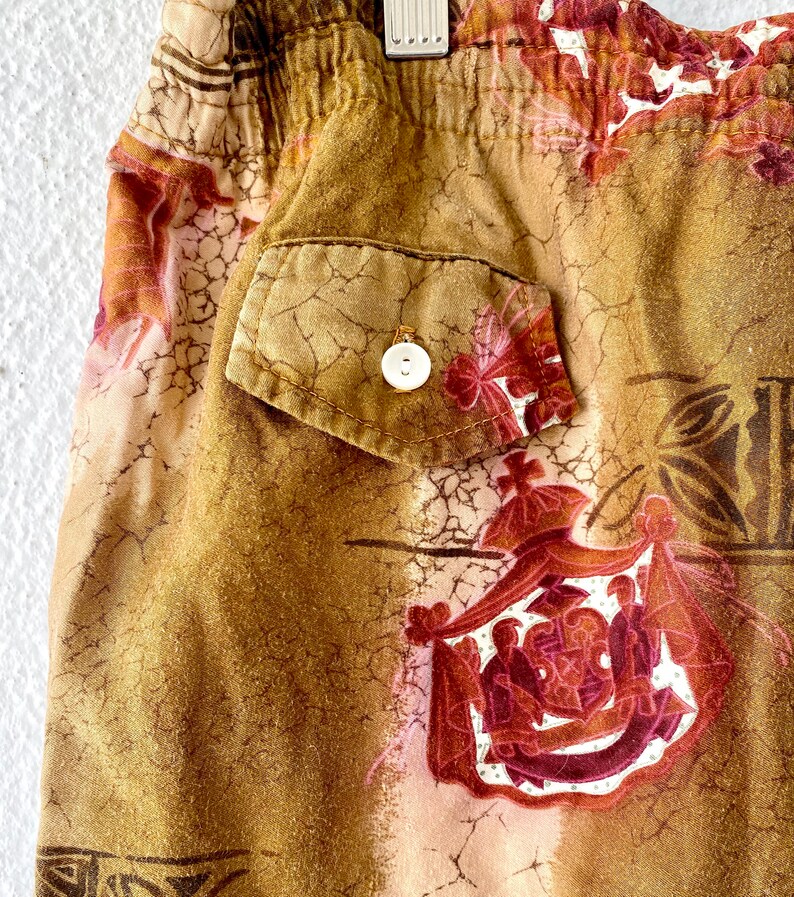 May include: Close-up of a pair of shorts with an elastic waistband and a single pocket. The shorts feature a brown and tan floral pattern with a white button on the pocket. The fabric has a textured appearance.