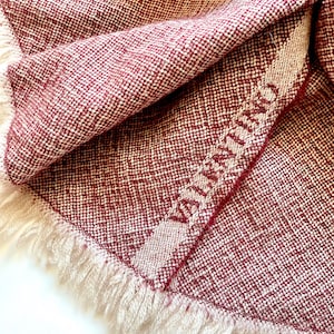May include: A burgundy and white woven throw blanket with a fringe border. The blanket has the word "Warmth" woven into the fabric.