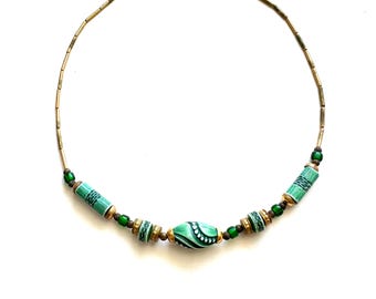 Puede incluir: Un collar verde y dorado con una gran cuenta verde y blanca con patrón en el centro.