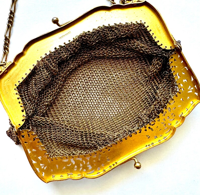 Pu&ograve; includere: Una borsa a rete metallica dorata con un design decorativo traforato. La borsa ha una tracolla a catena e una chiusura a scatto.
