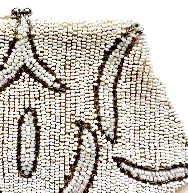 May include: A white beaded clutch bag with a floral design. The beads are small and closely spaced, creating a smooth, textured surface.