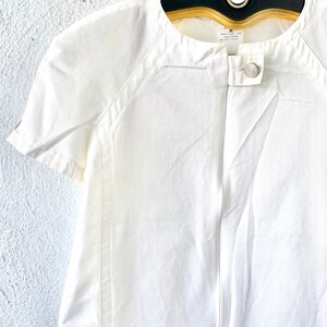 May include: White short-sleeved collared shirt with a single button closure. The shirt has a slightly fitted silhouette and a relaxed collar.
