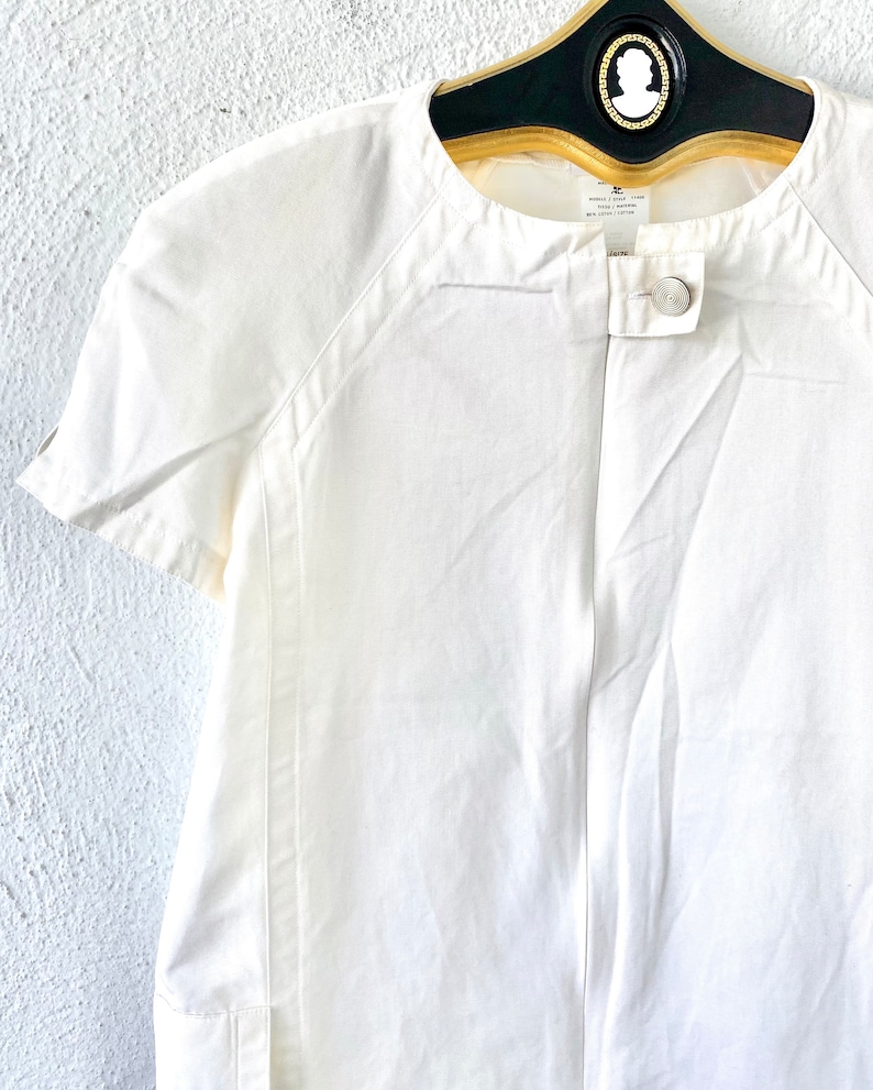 May include: White short-sleeved collared shirt with a single button closure. The shirt has a slightly fitted silhouette and a relaxed collar.