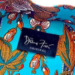May include: A close-up of a turquoise fabric with a paisley pattern in shades of orange, brown, and green. A black label with white text reads "Diane von Furstenberg ORIGINAL".