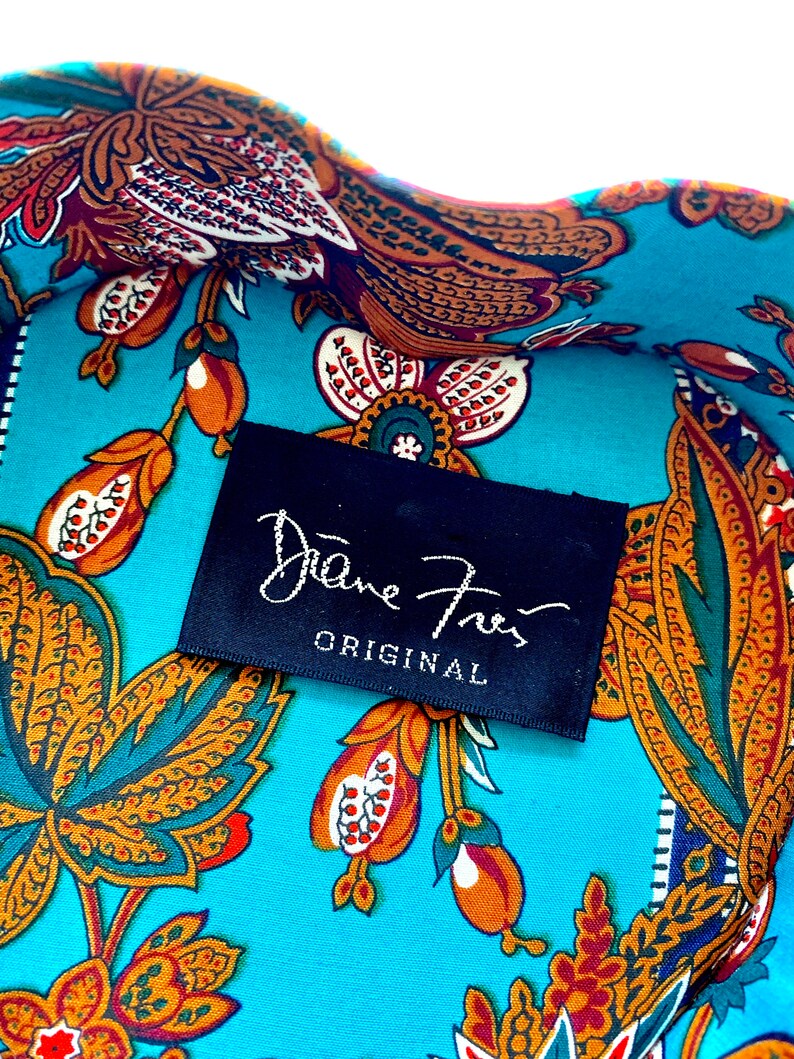 May include: A close-up of a turquoise fabric with a paisley pattern in shades of orange, brown, and green. A black label with white text reads "Diane von Furstenberg ORIGINAL".
