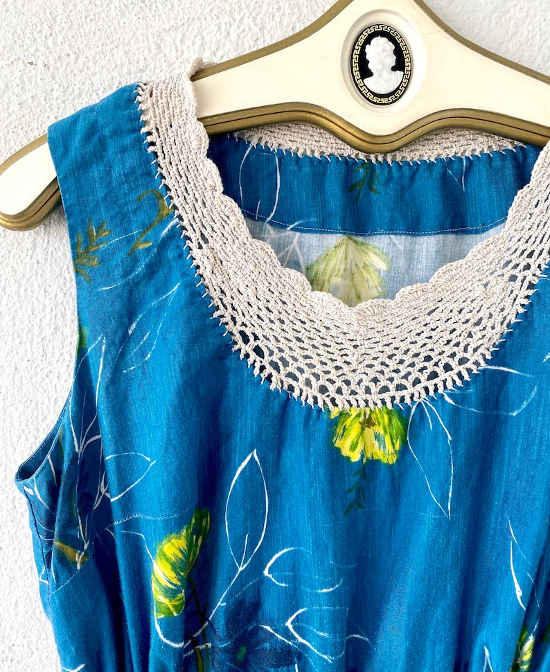 May include: A sleeveless blue dress with a white crochet neckline and a floral print. The dress has a fitted bodice and a flowing skirt.