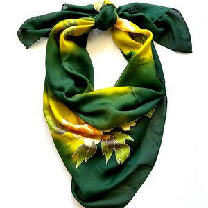 K&ouml;nnte beinhalten: Ein gr&uuml;ner und gelber Seidenschal mit einem Blumenmuster. Der Schal ist zu einem Knoten gebunden und die Enden h&auml;ngen herunter.