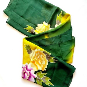 K&ouml;nnte beinhalten: Ein gr&uuml;ner und gelber Seidenschal mit Blumenmuster. Die Blumen sind gelb, rosa und lila.
