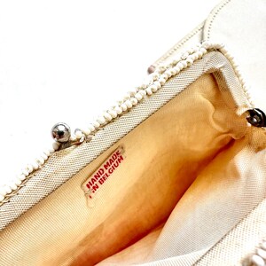 May include: White beaded clutch purse with a silver clasp and a red label that reads "HAND MADE IN BELGIUM".