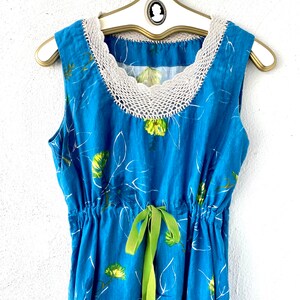 May include: A blue sleeveless dress with a white crochet neckline and a green ribbon tie at the waist. The dress has a floral print with white outlines.