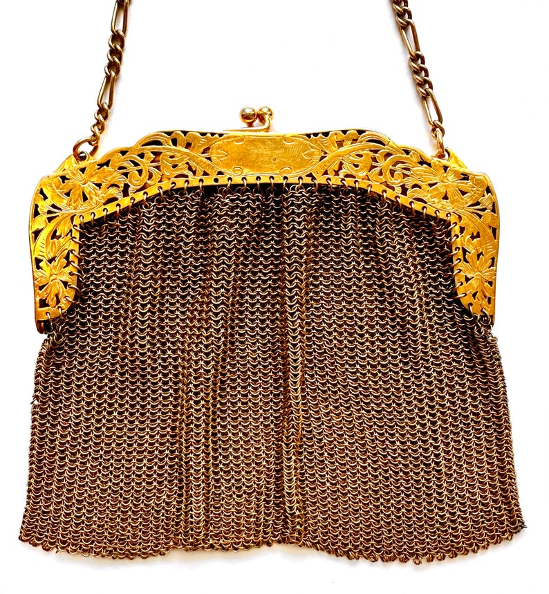 Pu&ograve; includere: Una borsa a rete di catena dorata con una chiusura decorativa in metallo dorato ornata. La chiusura ha un motivo floreale.