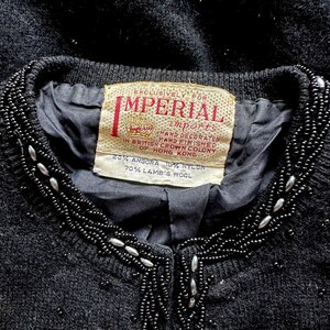 Puede incluir: Un c&aacute;rdigan negro con un cuello de cuentas. La etiqueta dice "Exclusively for Imperial Imports" y "20% Angora 10% Nylon 70% Lamb's Wool".