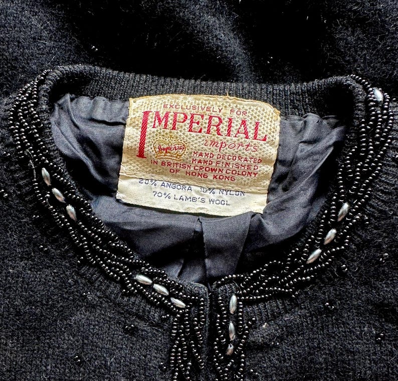 Puede incluir: Un c&aacute;rdigan negro con un cuello de cuentas. La etiqueta dice "Exclusively for Imperial Imports" y "20% Angora 10% Nylon 70% Lamb's Wool".