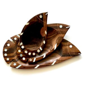 Puede incluir: Un juego de tres platos de servir de madera con forma de pez con incrustaciones de nácar. Los platos están anidados, con el plato más pequeño en la parte superior.