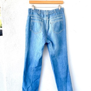 May include: A pair of light blue denim jeans hanging on a wooden hanger. The jeans have a straight leg and a classic five-pocket design.