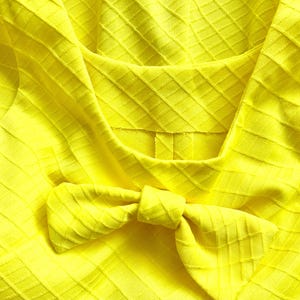Pu&ograve; includere: Un tessuto giallo brillante con un motivo a rombi e un fiocco legato al centro.