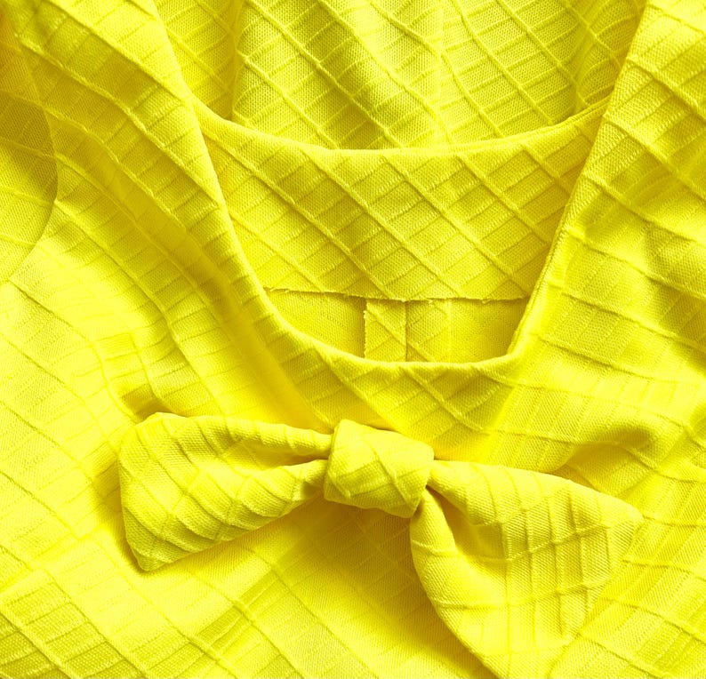 Pu&ograve; includere: Un tessuto giallo brillante con un motivo a rombi e un fiocco legato al centro.