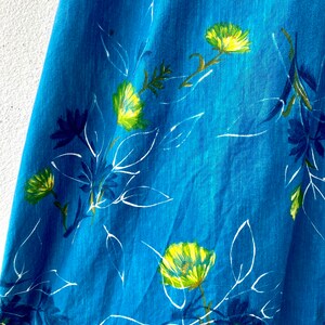 May include: A close-up of a blue fabric with a white and yellow floral pattern. The fabric has a textured surface and a slightly faded look.