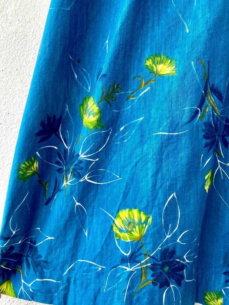 May include: A close-up of a blue fabric with a white and yellow floral pattern. The fabric has a textured surface and a slightly faded look.