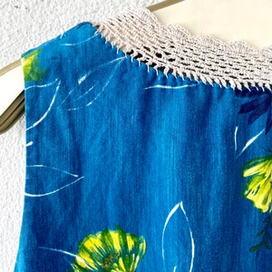 May include: A sleeveless blue dress with a white crochet neckline and a floral print featuring yellow and green flowers.