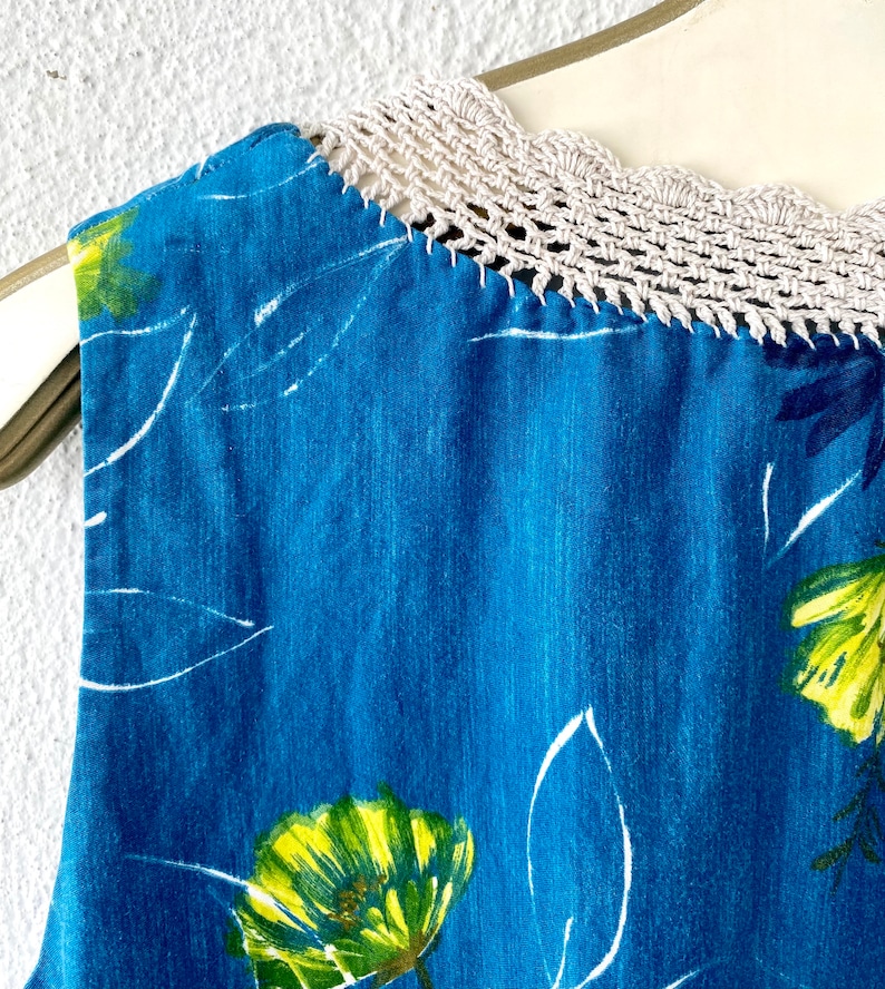 May include: A sleeveless blue dress with a white crochet neckline and a floral print featuring yellow and green flowers.