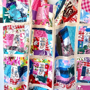 May include: A patchwork quilt made from colorful fabric scraps. The quilt is made in a square pattern with a variety of floral and geometric prints. The quilt is a vibrant mix of pink, blue, green, and red.