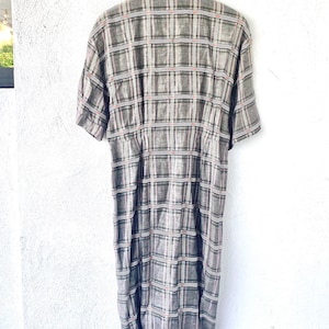 May include: A short-sleeved dress featuring a grey, black, and white plaid pattern with thin red accent lines. The garment has a collared neckline, a button-down front, and a fitted waistline that transitions into a straight skirt silhouette.
