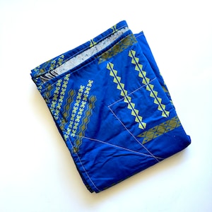 以下が含まれることがあります： 幾何学模様の青と緑の布地。布地は半分に折り畳まれ、白い背景になっています。