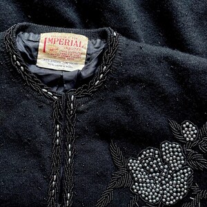Puede incluir: Un c&aacute;rdigan negro de punto con cuello y dise&ntilde;o floral de cuentas. La etiqueta dice "Exclusively for Imperial Imports Hand Decorated in British Crown Colony of Hong Kong 20% Angora 20% Nylon 70% Lamb's Wool."