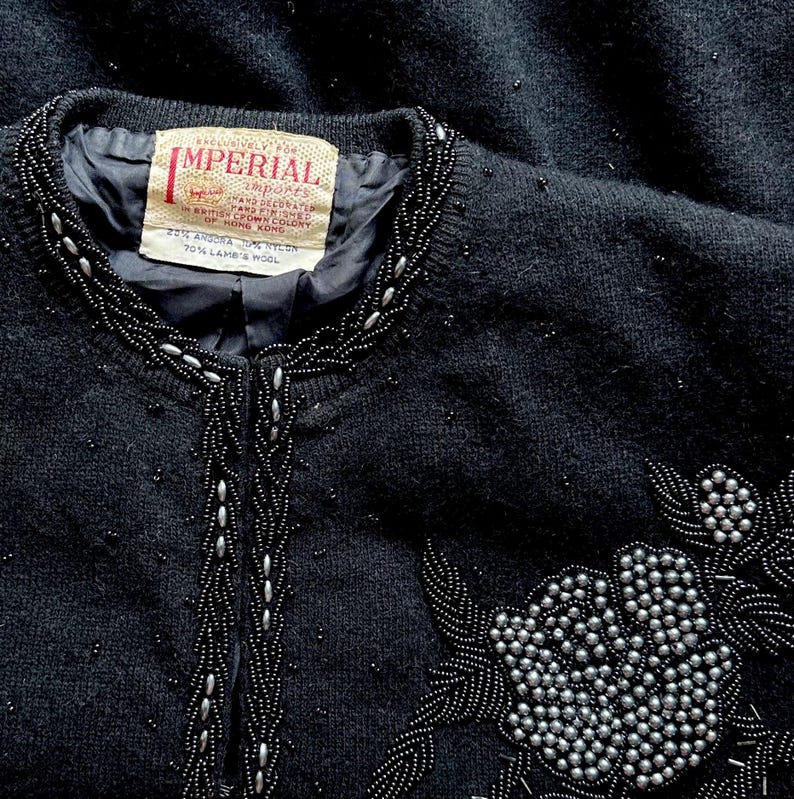 Puede incluir: Un c&aacute;rdigan negro de punto con cuello y dise&ntilde;o floral de cuentas. La etiqueta dice "Exclusively for Imperial Imports Hand Decorated in British Crown Colony of Hong Kong 20% Angora 20% Nylon 70% Lamb's Wool."