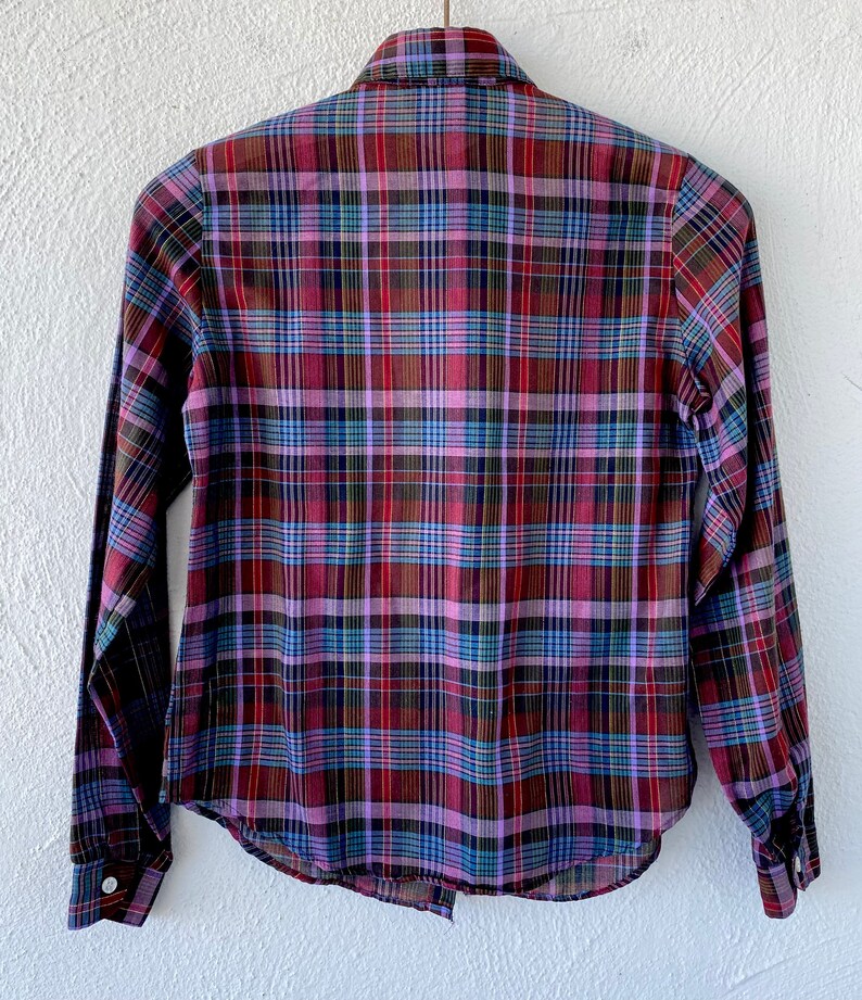 May include: A long-sleeved plaid shirt with a button-down collar. The shirt is a mix of red, purple, blue, and green plaid.