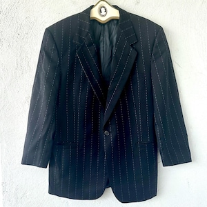 Peut inclure: Un blazer noir avec un motif discret de fines rayures blanches, une fermeture &agrave; un bouton, des revers crant&eacute;s et des manches longues. Le v&ecirc;tement est pr&eacute;sent&eacute; sur un cintre avec un d&eacute;tail cam&eacute;e au col, affichant une coupe structur&eacute;e.