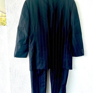 Peut inclure: Un costume bleu marine fonc&eacute; avec un motif &agrave; fines rayures blanches. L'ensemble comprend un blazer &agrave; manches longues avec un revers crant&eacute; et des boutons aux poignets, assorti &agrave; un pantalon &agrave; coupe droite avec des ourlets &agrave; revers.