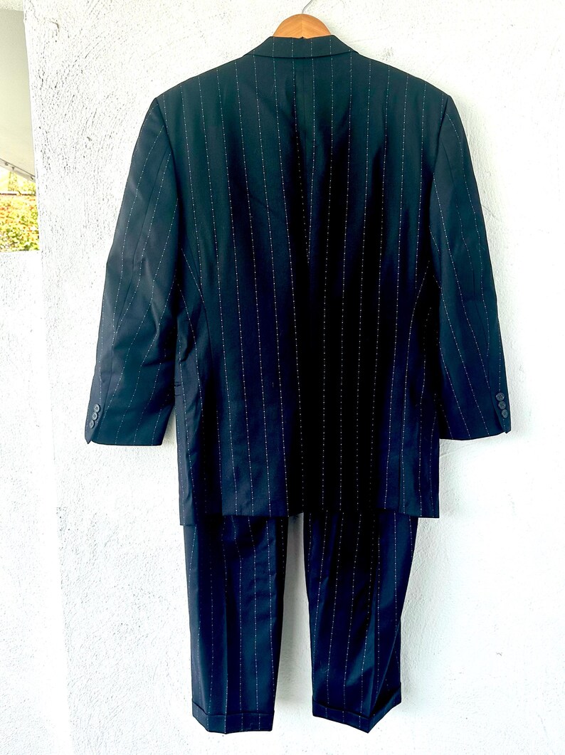 Peut inclure: Un costume bleu marine fonc&eacute; avec un motif &agrave; fines rayures blanches. L'ensemble comprend un blazer &agrave; manches longues avec un revers crant&eacute; et des boutons aux poignets, assorti &agrave; un pantalon &agrave; coupe droite avec des ourlets &agrave; revers.