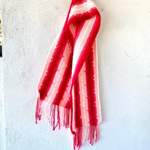 May include: A pink and white striped crocheted scarf with fringe on the ends.