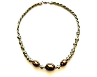 May include: A green braided cord necklace with three large, oval-shaped, brown beads.