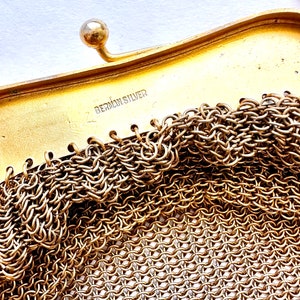 Pu&ograve; includere: Primo piano di una borsa a rete dorata con una chiusura e le parole "German Silver" stampate all'interno.