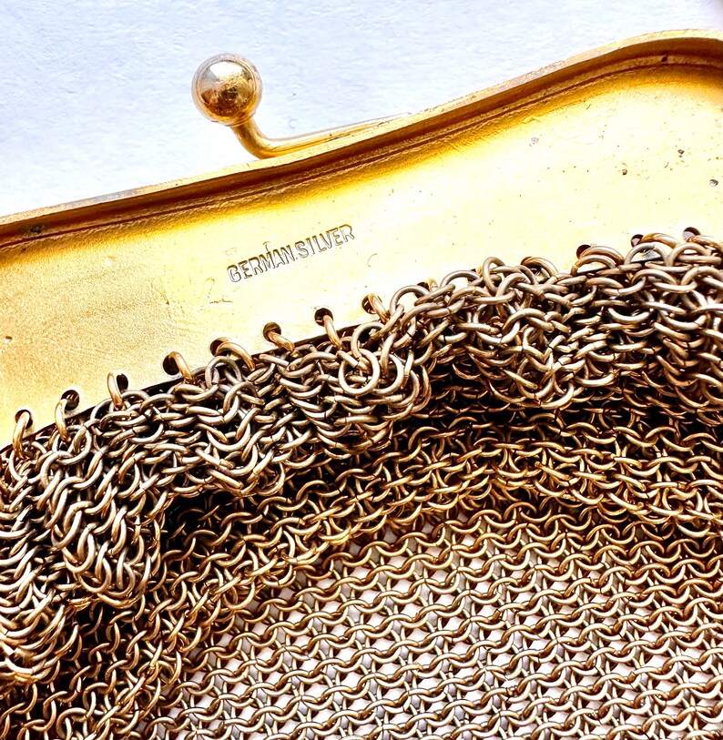Pu&ograve; includere: Primo piano di una borsa a rete dorata con una chiusura e le parole "German Silver" stampate all'interno.