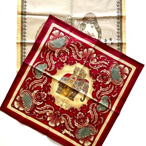 May include: Two silk scarves with elephant designs. One scarf is a deep red with gold floral patterns and an elephant illustration. The other is a cream color with a border and an elephant illustration. Both scarves are square.