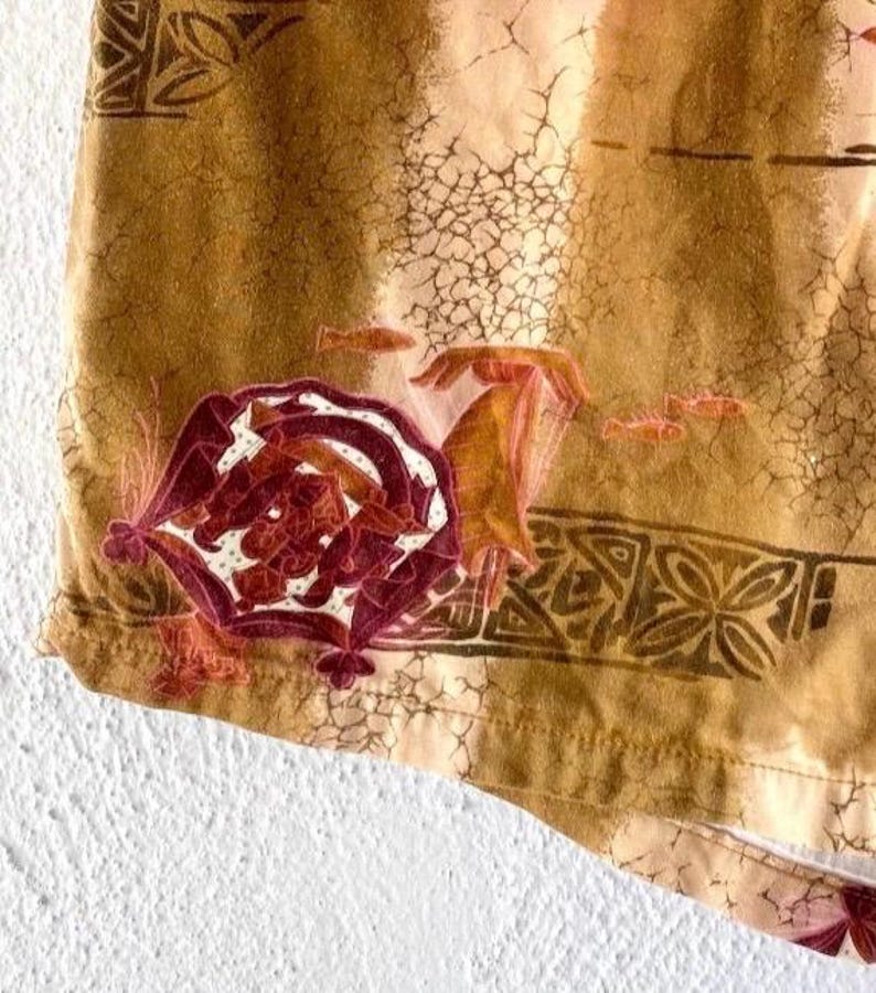 May include: Close-up of a section of fabric with a warm, earthy color palette. The design features a large, ornate floral motif in shades of burgundy and white, with smaller fish and geometric patterns. The fabric has a textured, aged appearance.