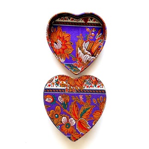 May include: A purple heart-shaped box with a floral pattern in shades of orange, green, and white. The box is open, revealing the inside of the box.