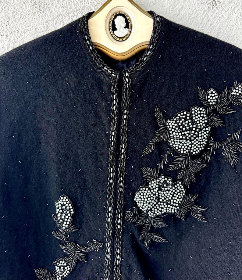 Puede incluir: Una chaqueta de lana negra con ribete de cuentas y dise&ntilde;o floral. Las flores est&aacute;n hechas de cuentas blancas y est&aacute;n bordadas en la chaqueta.