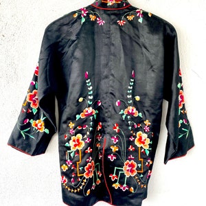 Puede incluir: Una chaqueta de seda negra con cuello mandar&iacute;n y bordado floral intrincado en tonos de rojo, rosa, verde y amarillo.
