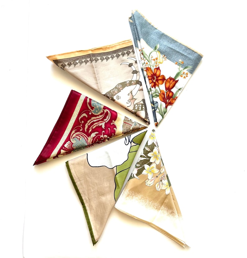 May include: An assortment of colorful silk scarves arranged in a starburst pattern. The scarves feature various designs, including floral patterns, ornate scrollwork, and a beige scarf with a decorative border and a figure. The color palette includes red, blue, beige, and green.