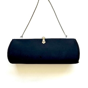 May include: A black satin evening bag with a silver chain strap. The rectangular clutch features a decorative clasp with sparkling rhinestones. The bag is a classic accessory for formal events.