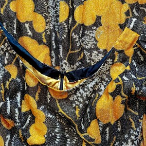 May include: Close-up of a black and gold fabric with a floral pattern. The fabric has a shimmery texture and features a zipper detail.