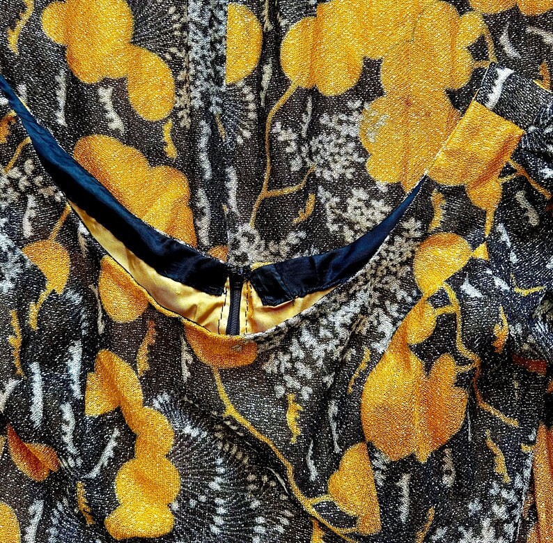 May include: Close-up of a black and gold fabric with a floral pattern. The fabric has a shimmery texture and features a zipper detail.